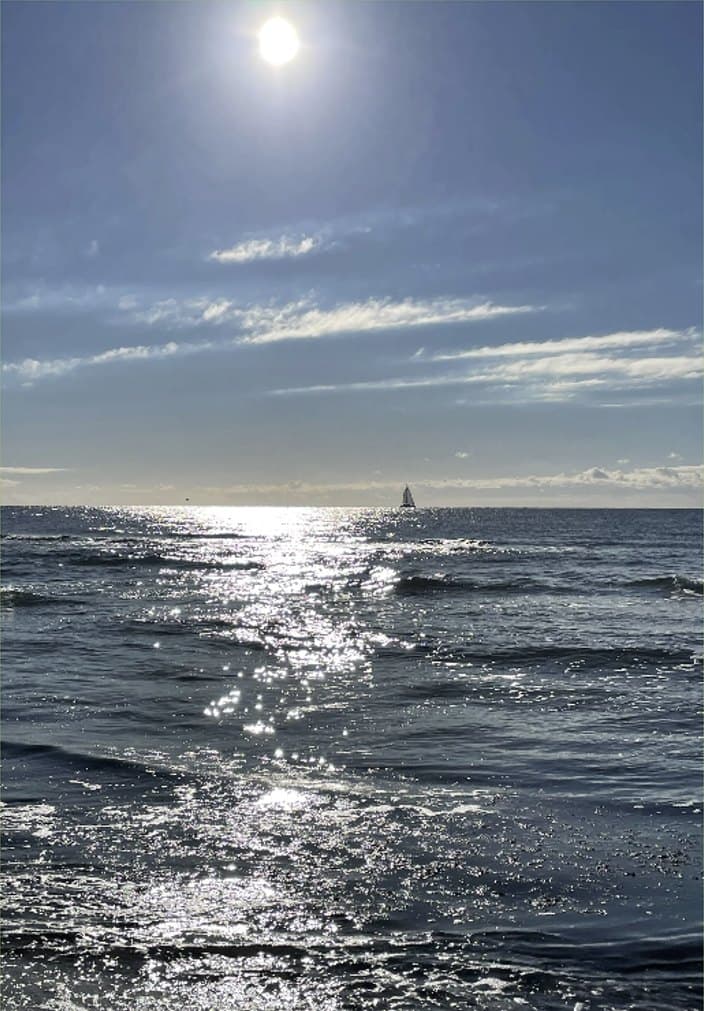 Sun over the sea with a sailing boat on the horizon