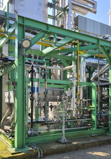 Green steel frame holding pipes and valves at a process plant